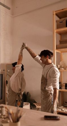 two men in aprons are standing near a table and one man is holding his arm up