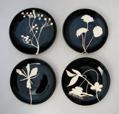 four black plates with white flowers and leaves painted on the front, side, and back