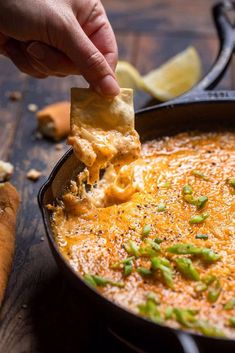 a hand dipping a tortilla chip into a bowl of dip with cheese and green peppers