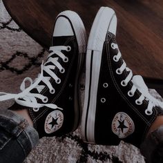 someone wearing black and white converse shoes sitting on the floor