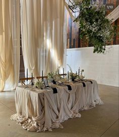 the table is covered with white cloths and black sashes, surrounded by greenery