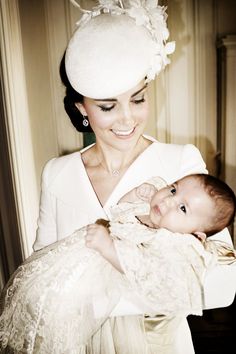 a woman holding a baby wearing a white dress and hat with feathers on it's head