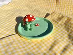 a green plate with a red mushroom on it sitting on a yellow and white checkered tablecloth