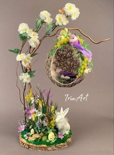 an easter decoration with white flowers and purple birds in a nest on a tree branch