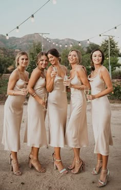 the bridesmaids are all dressed in beige dresses and holding champagne glasses for each other