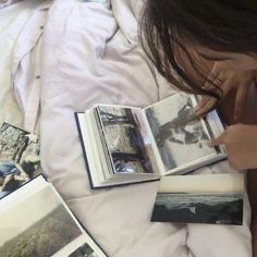 a person laying in bed with an open book and several pictures on the floor next to them