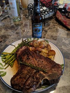 a plate with steak, potatoes and asparagus next to a bottle of beer