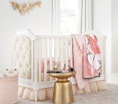 a white crib with pink and gold decor in the corner next to a baby's bed