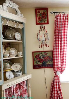 a red and white checkered curtain hanging on the side of a wall next to a china cabinet