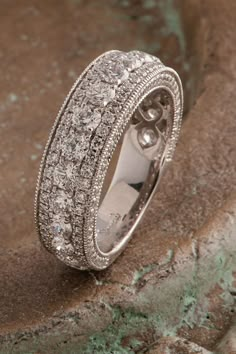 a wedding ring with diamonds on top of it sitting on a stone slab in front of a rock