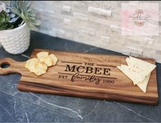 a wooden cutting board with cheese and crackers on it next to a potted plant