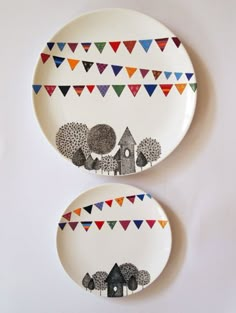 two plates with trees and houses painted on them are hanging on the wall next to each other