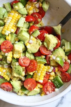 a white bowl filled with corn, tomatoes and avocado