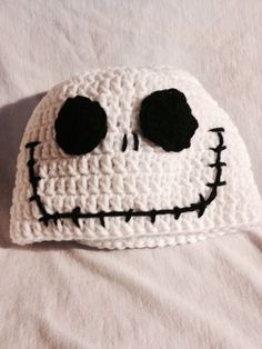 a crocheted skull hat with black eyes and mouth is laying on a white sheet