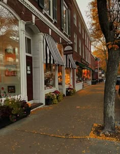 an empty sidewalk in front of a store with autumn leaves on the ground and parked cars