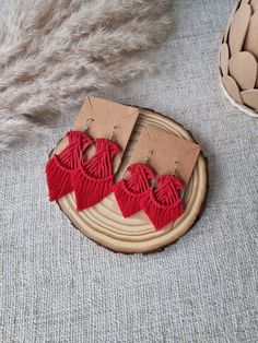 two red earrings with fringes are sitting on a piece of cardboard next to some feathers