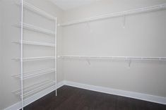 an empty walk in closet with white shelving and wood flooring on the walls