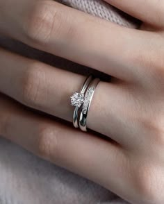 a woman's hand with two wedding rings on her left and the other hand holding an engagement ring