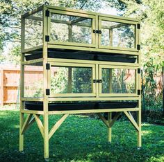 a large green bird cage sitting on top of a grass covered field next to trees