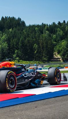 a red and yellow race car driving on a track with trees in the back ground