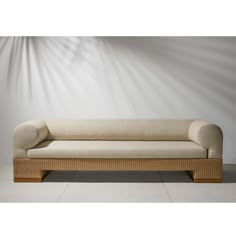 a beige couch sitting on top of a white floor next to a wall with light coming through it