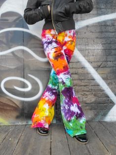 a woman standing in front of a wall wearing colorful pants and a black leather jacket