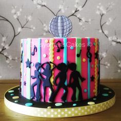 a colorful birthday cake decorated with music notes and dancing silhouettes on a wooden table