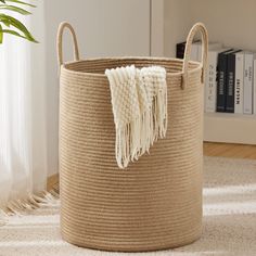 a large round storage basket with tassels and handles on the floor next to a plant