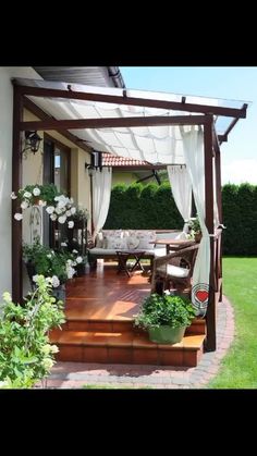 an outdoor patio with white curtains and flowers on the steps leading up to the deck