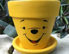 a yellow planter with a face painted on it's side sitting on a rock