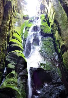 there is a waterfall in the middle of some mossy rocks with water running down it