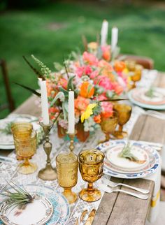 the table is set with plates, candles and flowers in vases on top of it