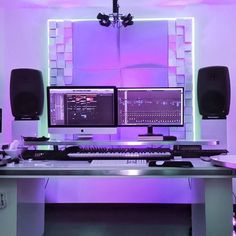 a computer desk with two monitors and speakers on it in front of a purple wall