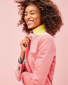 a woman with curly hair wearing a pink jacket and smiling at the camera while standing against a pink background