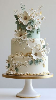 a three tiered wedding cake with white flowers on the top and gold trimmings