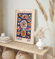 a wooden table topped with baskets and vases next to a framed art print on the wall