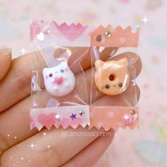 there are two small plastic cats in the package on someone's hand and one is wearing a pink bow