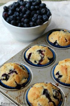 blueberry muffins sitting in a pan next to a bowl of berries