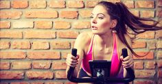 a woman on a stationary exercise bike in front of a brick wall with her hair blowing in the wind