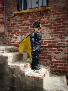 a young boy dressed as a superhero standing on steps with his cape draped over his face