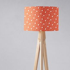 an orange and white polka dot lampshade with wooden tripod legs on grey background