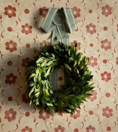 a green wreath sitting on top of a table next to a wallpaper covered with flowers