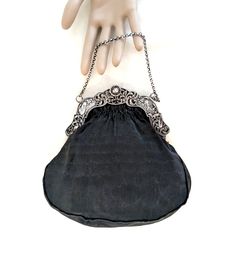 A black handbag with a Dutch 2nd standard silver (.833 purity), repousse frame with windmills, birds, a baby's face, and a cable chain handle.  The interior of the bag is hand sewn, taupe thick gauge, silk satin, and it has two small, side pockets.  The exterior silk is a finely ribbed matte black silk.  The handle drop is 3 1/2 inches, its overall dimensions are 7 1/2 H x 7 1/2 W x 1/2 D inches.  The bag dates from the late 19th to the first half of the 20th century. CONDITION:  Some signs of w Silver Handheld Evening Bag With Chain Strap, Handheld Silver Evening Bag With Chain Strap, Classic Silver Shoulder Bag With Chain Strap, Silver Bags With Detachable Handle For Events, Silver Formal Bag With Chain Strap, Classic Silver Shoulder Bag For Formal Occasions, Classic Silver Shoulder Bag For Formal Events, Elegant Silver Bag With Chain Strap, Luxury Silver Evening Bag With Detachable Handle