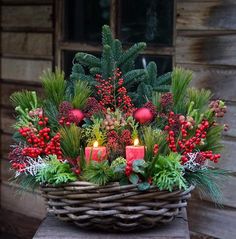 a basket filled with candles and greenery on top of a wooden table next to a building