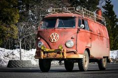 an old vw bus is parked on the street in front of snow covered trees