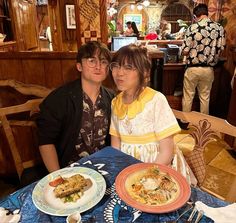 two people sitting at a table with plates of food in front of them, posing for the camera