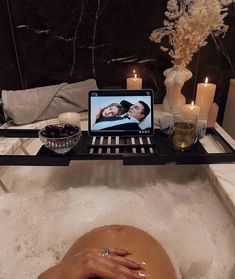 a woman laying in a bathtub with candles and a laptop on her lap top