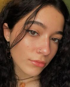 a close up of a person with curly hair and piercings on her nose wearing a necklace