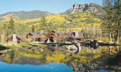 a lake in front of a mountain with houses on it and trees around the pond