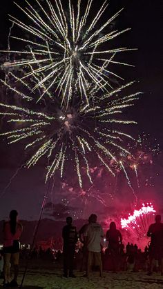 fireworks are lit up in the night sky with people standing on the beach watching them